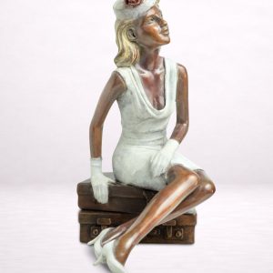 Sculpture en bronze d’une femme assise sur une valise, jambes croisées.