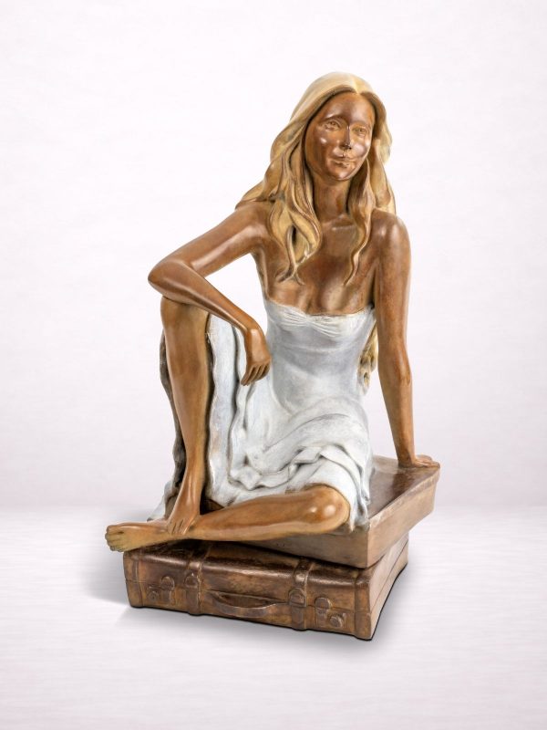 Sculpture en bronze d’une femme assise sur une valise, vue de face.