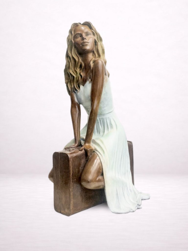 Sculpture en bronze d’une femme assise sur une valise, vue de trois-quarts.