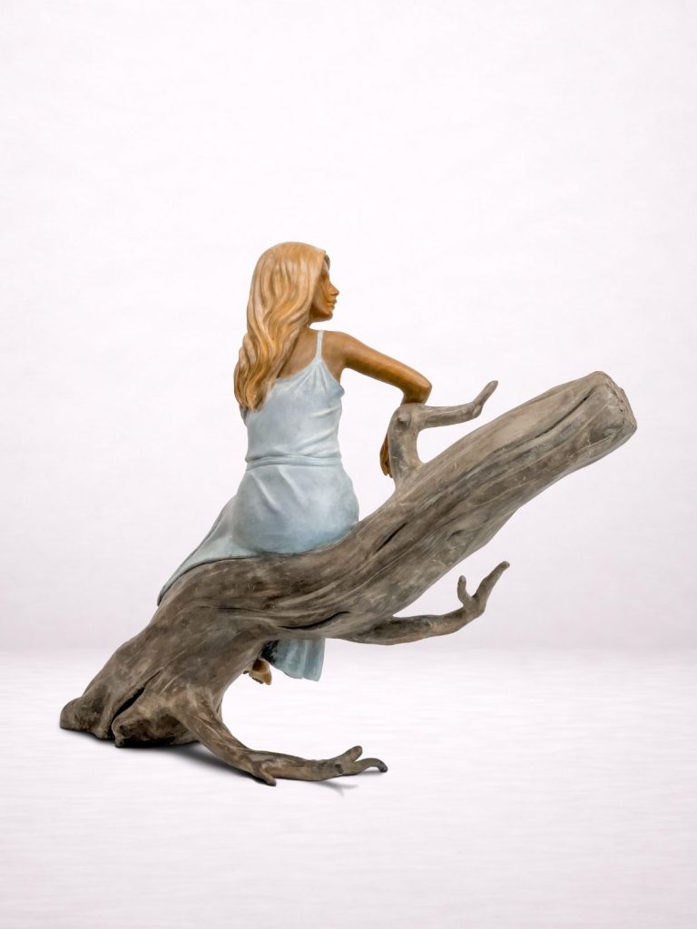 Sculpture en bronze d’une femme assise sur un tronc, vue trois-quarts arrière.