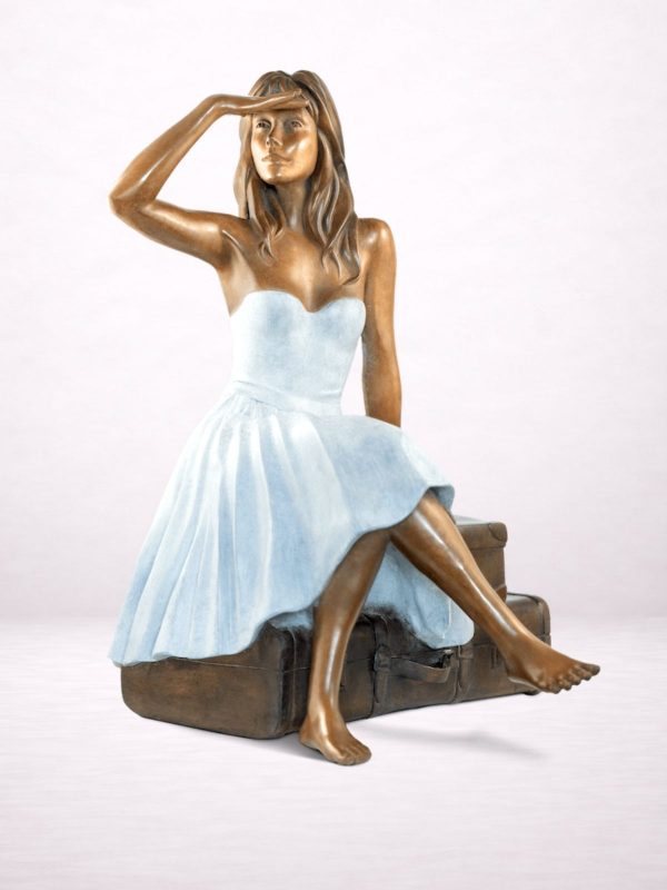 Sculpture en bronze d’une femme assise sur des valises, vue de trois-quarts avant.