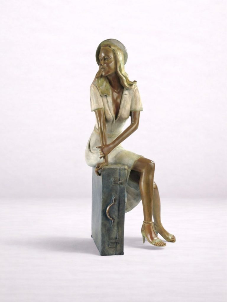 Sculpture en bronze d’une femme avec u béret assise sur une valise, vue de face.