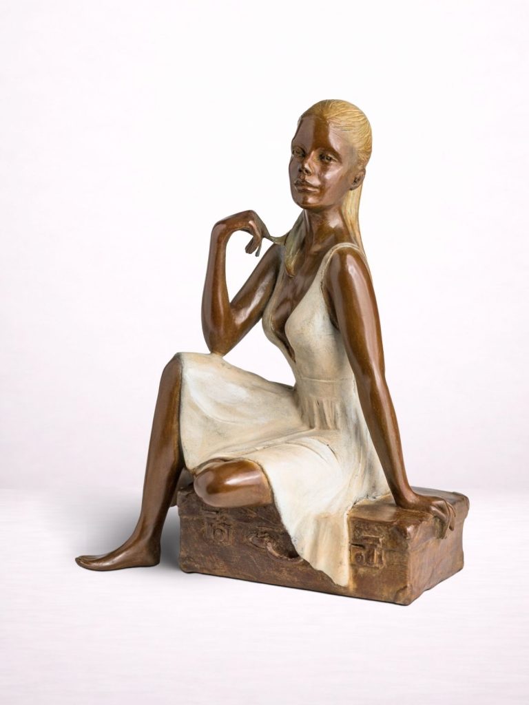 Sculpture en bronze d’une femme assise sur une valise, vue de face.