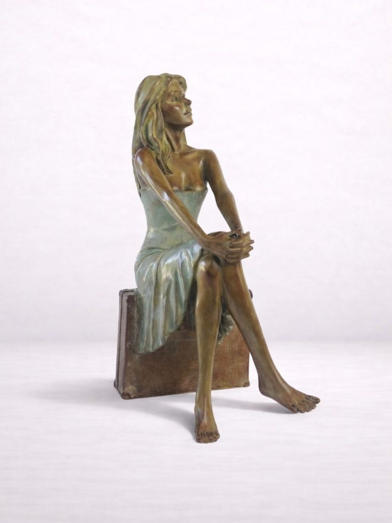Sculpture en bronze d’une femme assise sur une valise, mains croisées, vue de face.