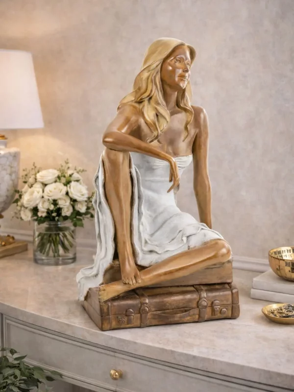 Sculpture en bronze d’une femme assise sur une valise, présentée dans un intérieur.