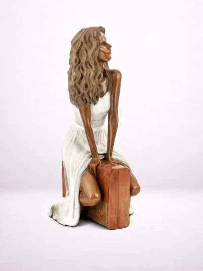 Sculpture en bronze d’une femme assise sur une valise, vue de face.