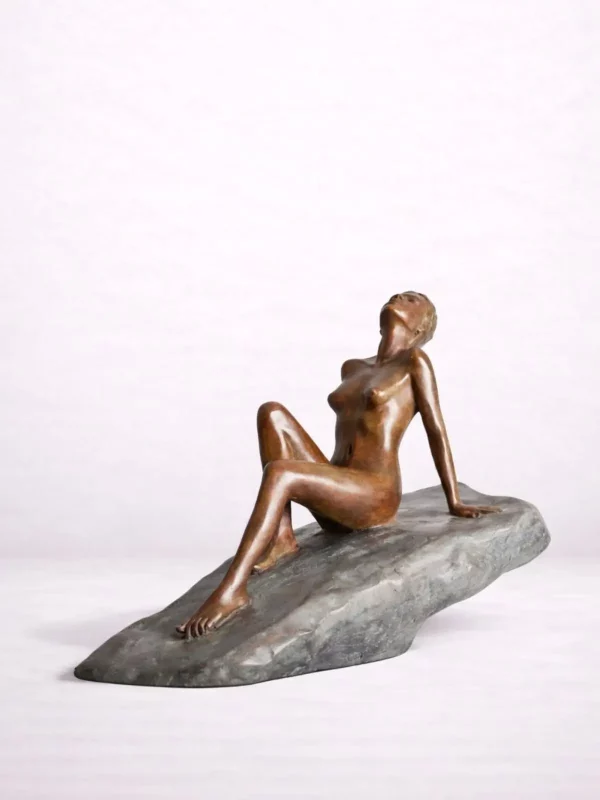 Sculpture en bronze d’une femme nue assise sur un rocher incliné.