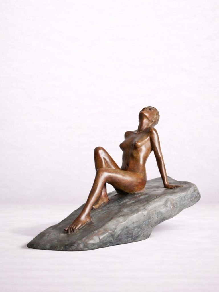 Sculpture en bronze d’une femme nue assise sur un rocher incliné.