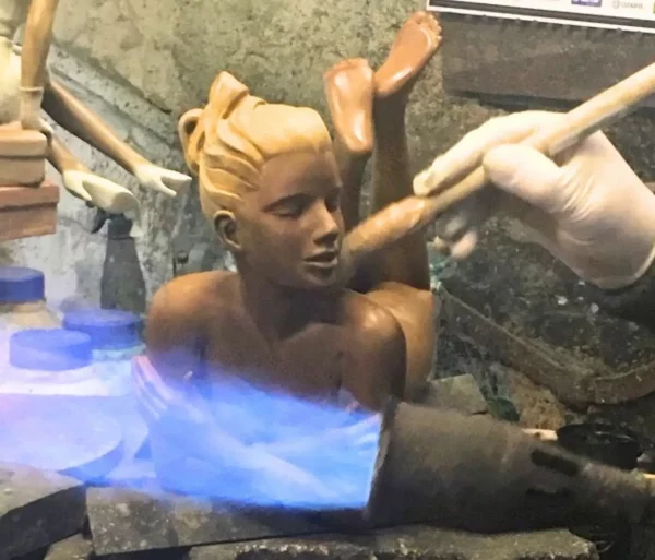 Application de patine sur une sculpture en bronze représentant une femme, avec une flamme de chalumeau et un pinceau.