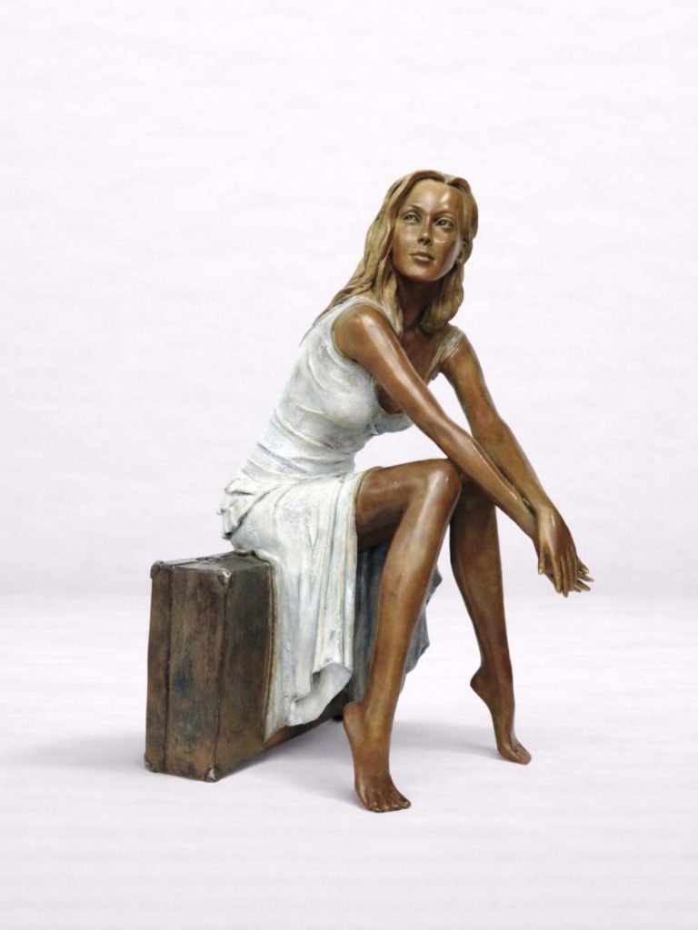 Sculpture en bronze d’une femme assise sur une valise, vue de profil.